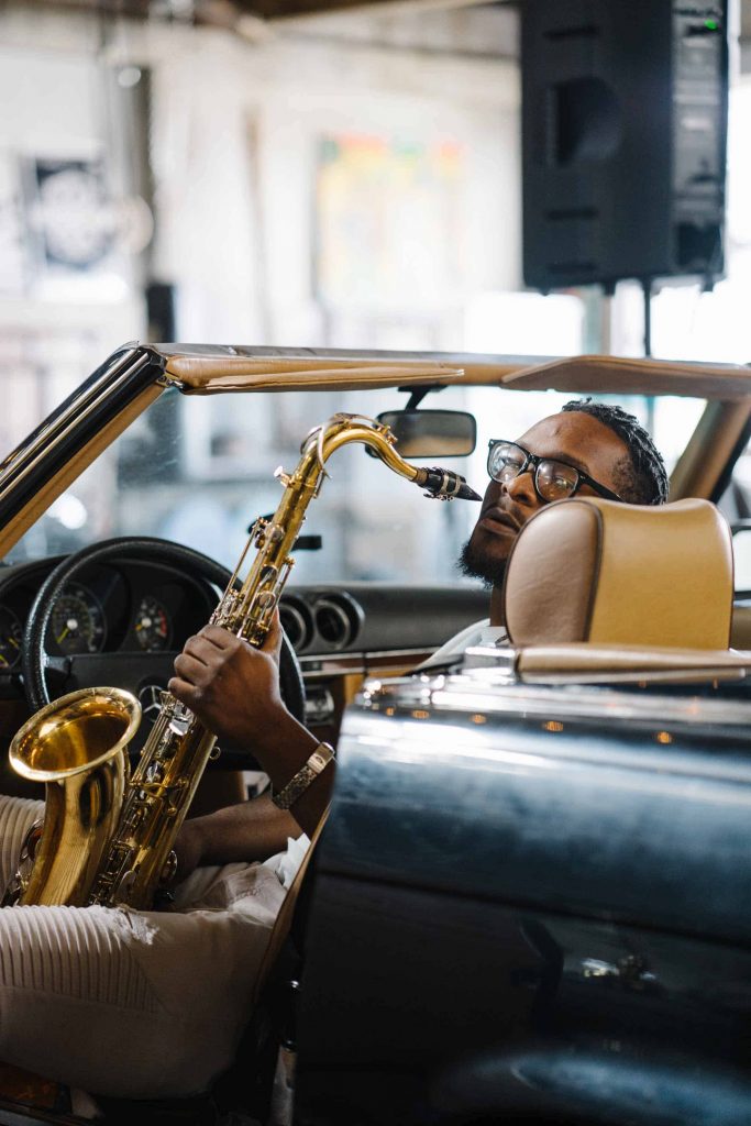 Josue Simon playing saxophone while sitting in the front seat of a car