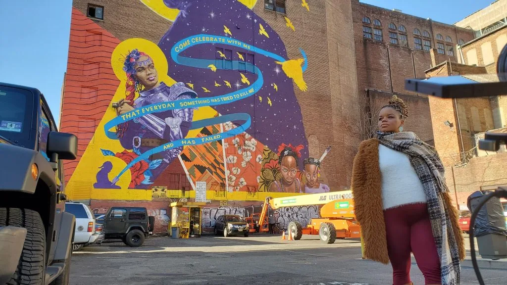 Poet and member of A Womb of Violet, Kween Moore, standing in front of Magnitude and Bond.